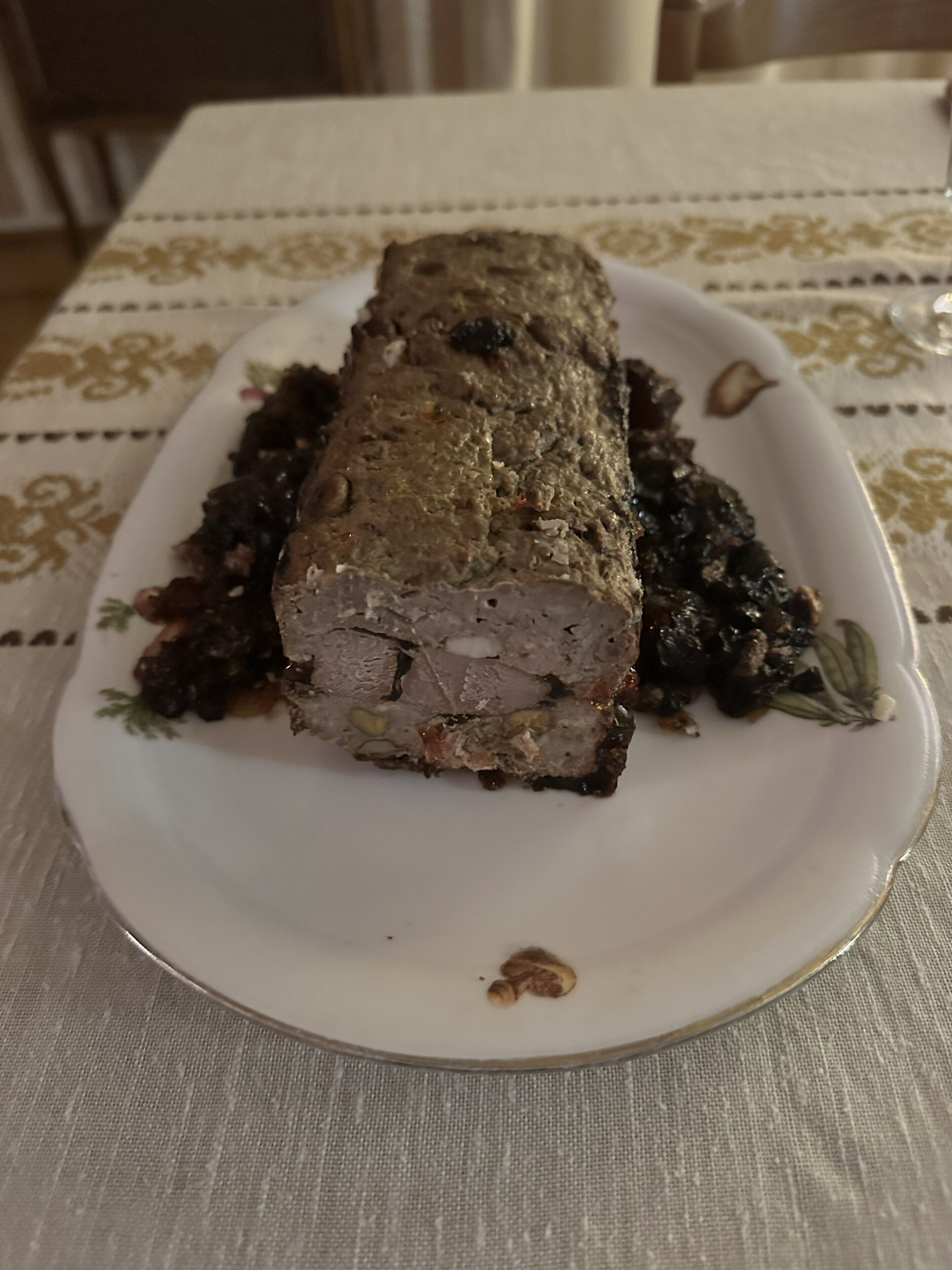 A plate with a meatloaf and greens on a tablecloth.