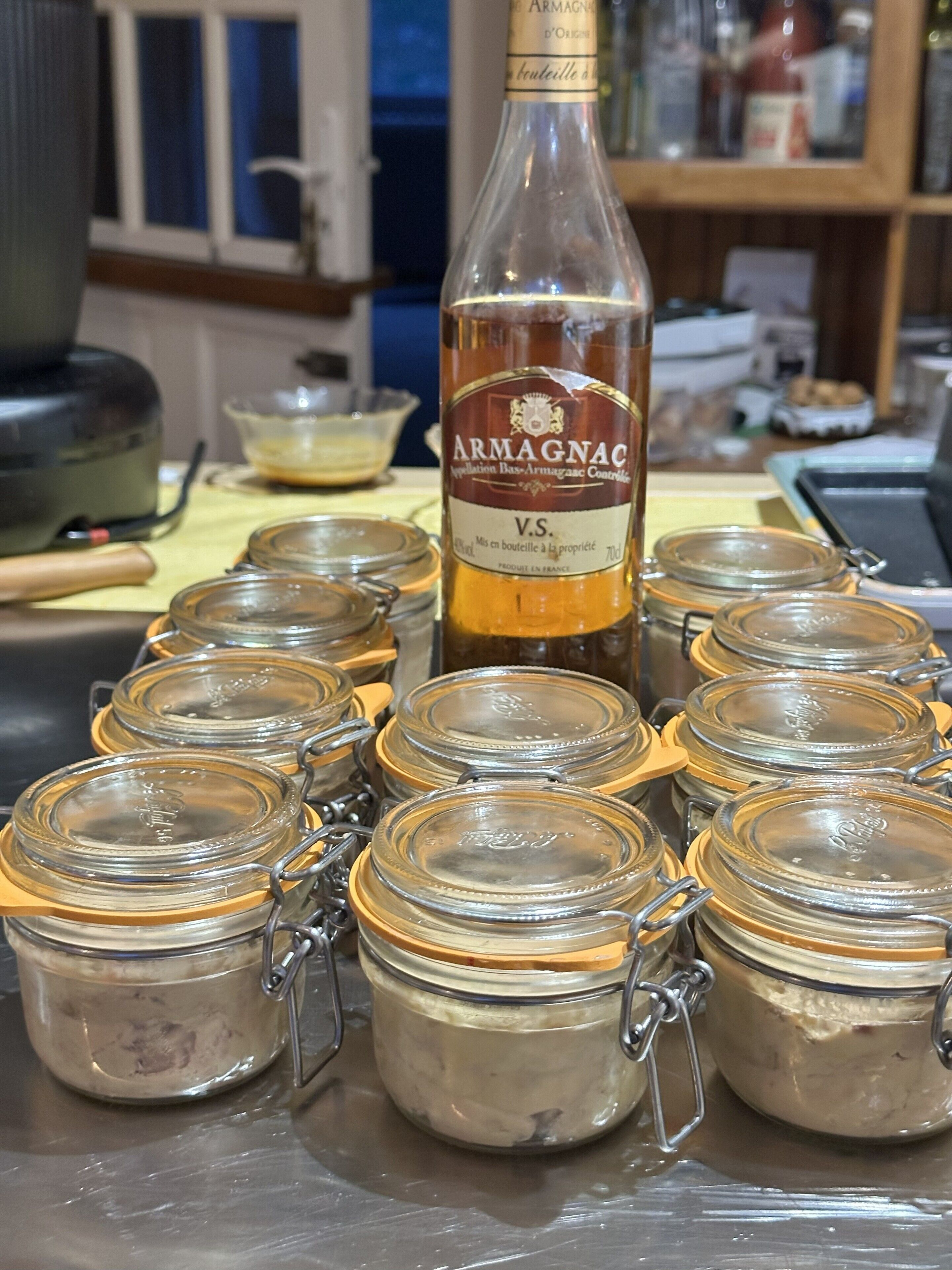 Eine Armagnac-Flasche und mehrere Glasbehälter mit Metalldeckeln auf einer Edelstahlfläche.