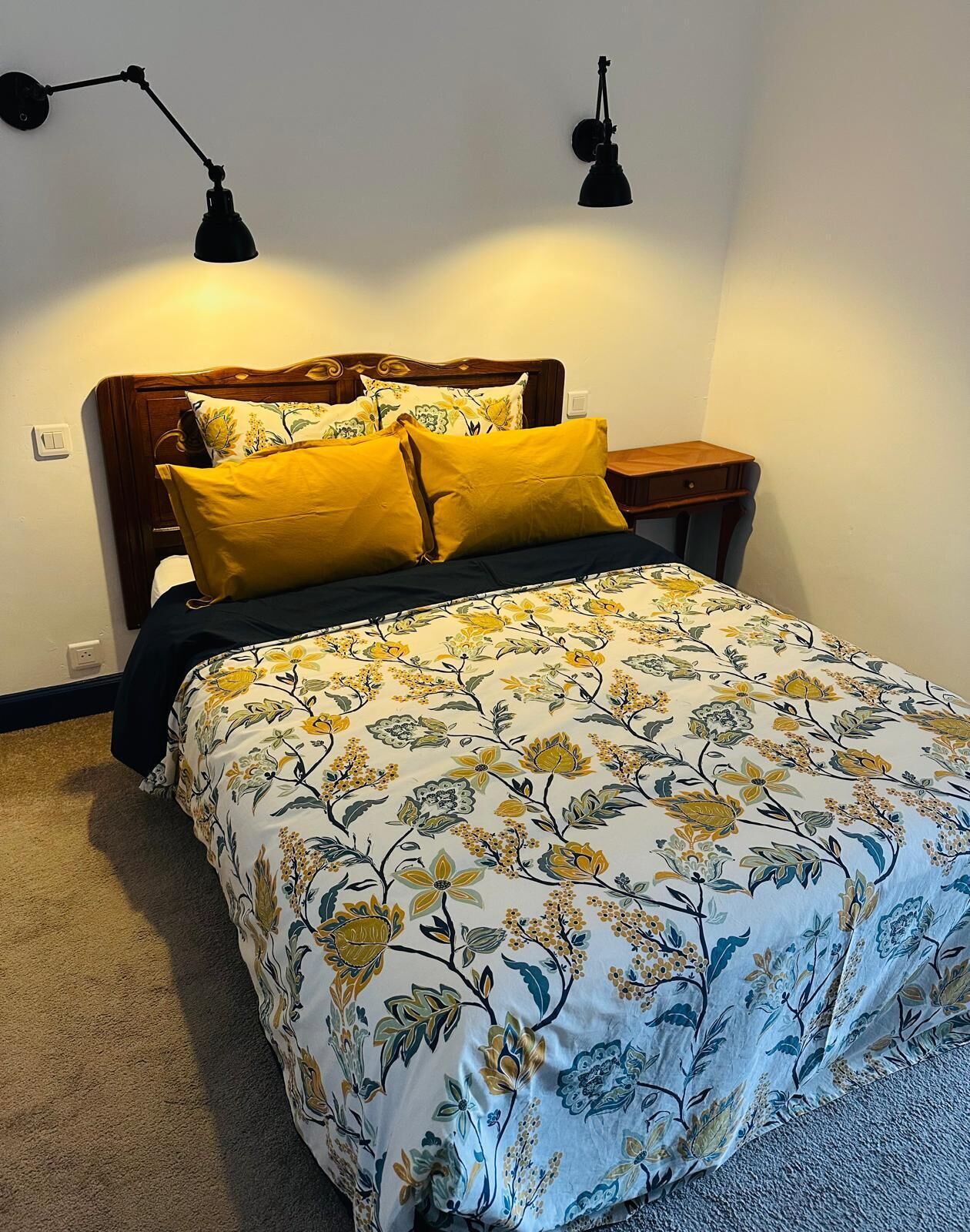 Un dormitorio con cama, dos lámparas de noche, una mesita de noche y una colcha estampada con motivos florales.