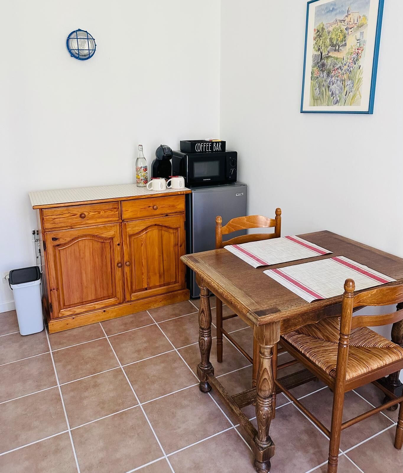 A compact kitchen with a wooden cabinet, a coffee maker, a microwave, and a dining table with chairs.