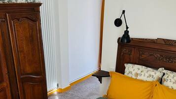A bedroom with a wooden wardrobe, a bed with floral bedding, a bedside table with a lamp, and a whiteboard on the wall.