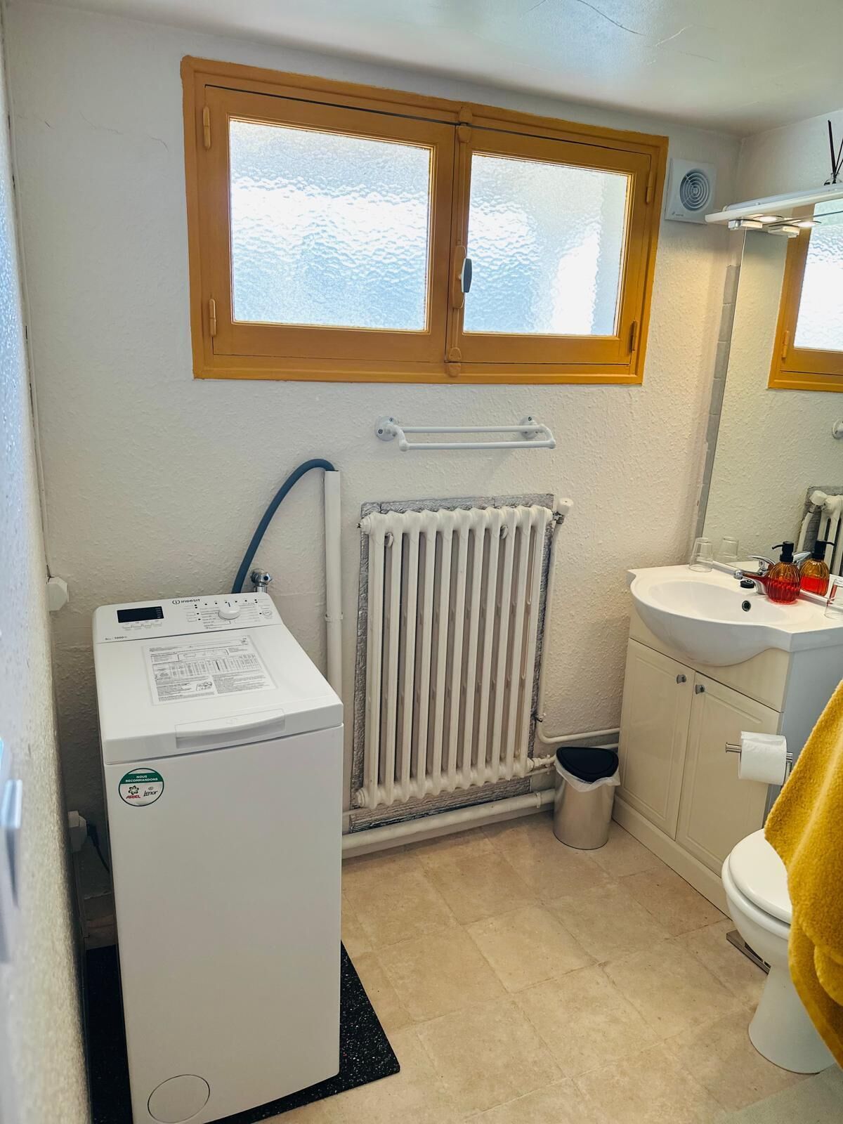A compact bathroom with a built-in washer, a radiator, a sink, and a toilet.