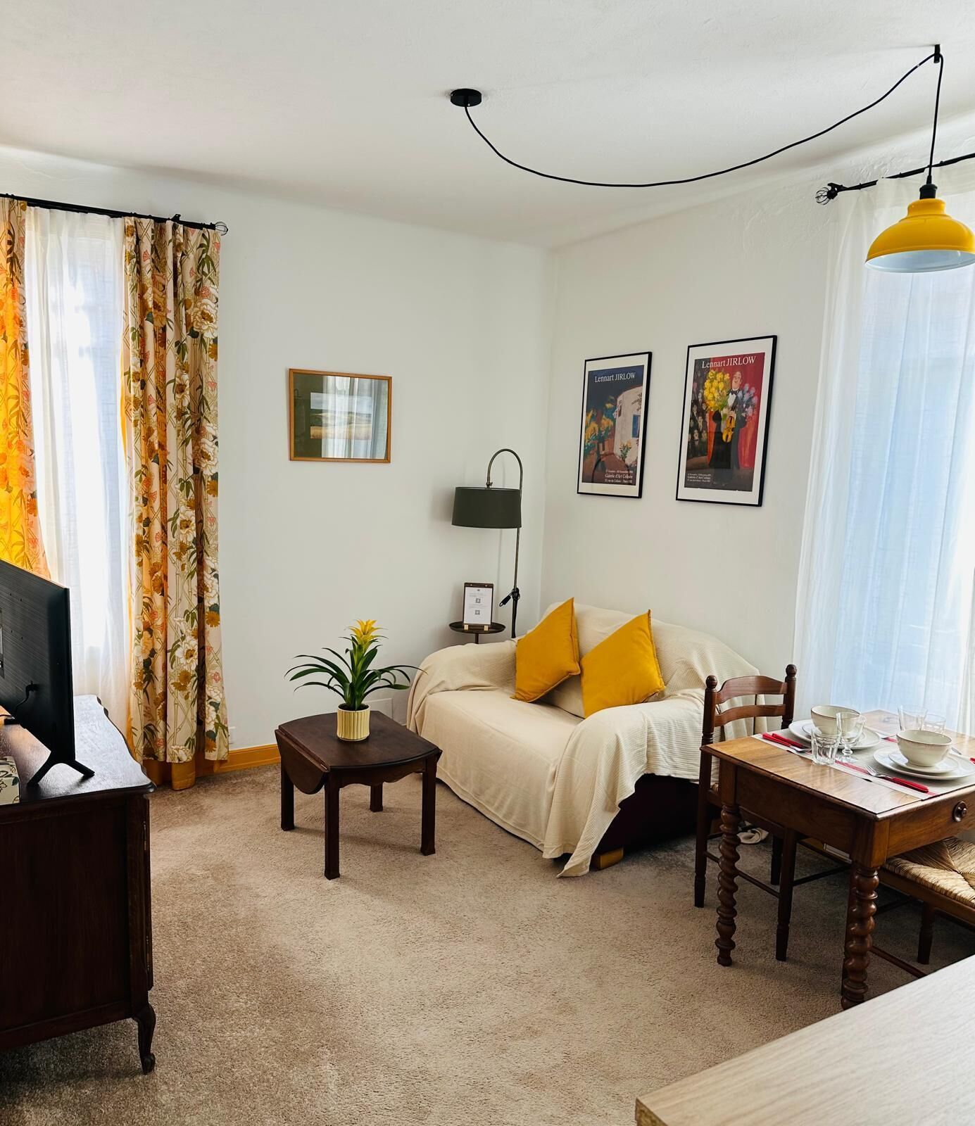 Un salon comprenant un canapé, une petite table avec une plante, un bureau avec un ordinateur et une table à manger avec des chaises.