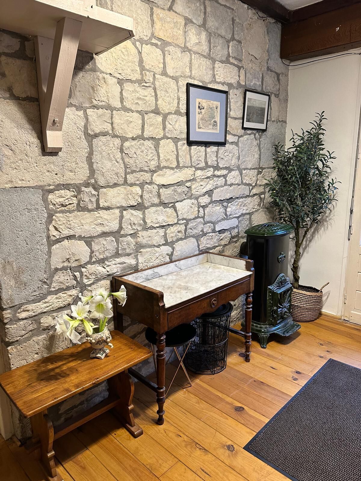 A rustic room with a stone wall, a wooden bench, a marble-top table, and a potted plant.