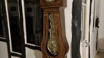 A tall grandfather clock with intricate carvings and a large face, positioned against a wall with a window and a door.