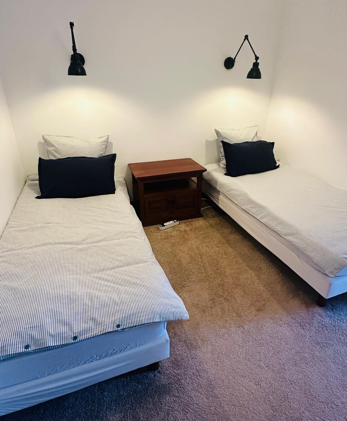 Una habitación con dos camas individuales, cada una con una almohada y una mesita de noche. Hay dos lámparas de pared.