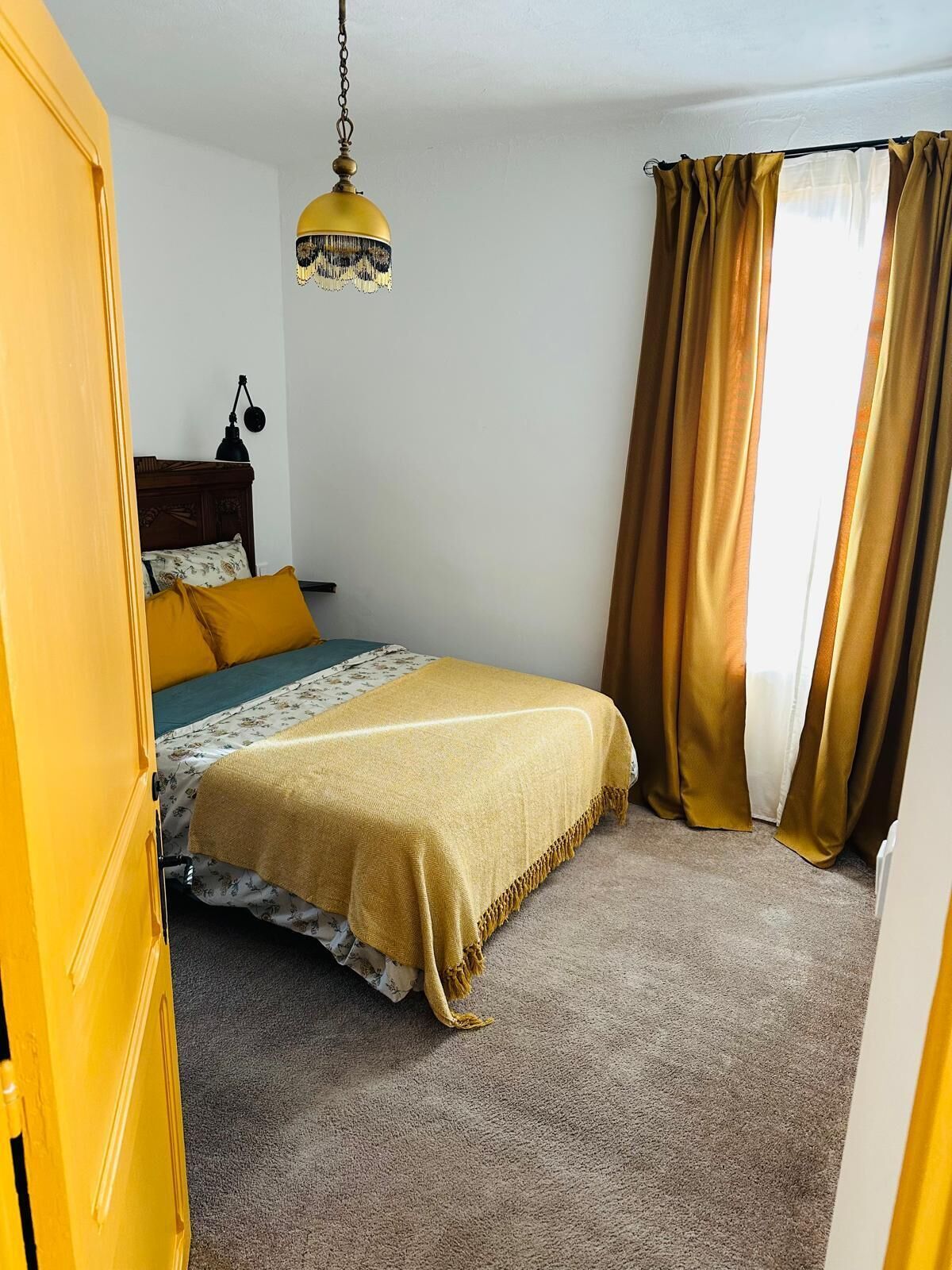 A bedroom with a bed, a hanging lamp, and curtains.