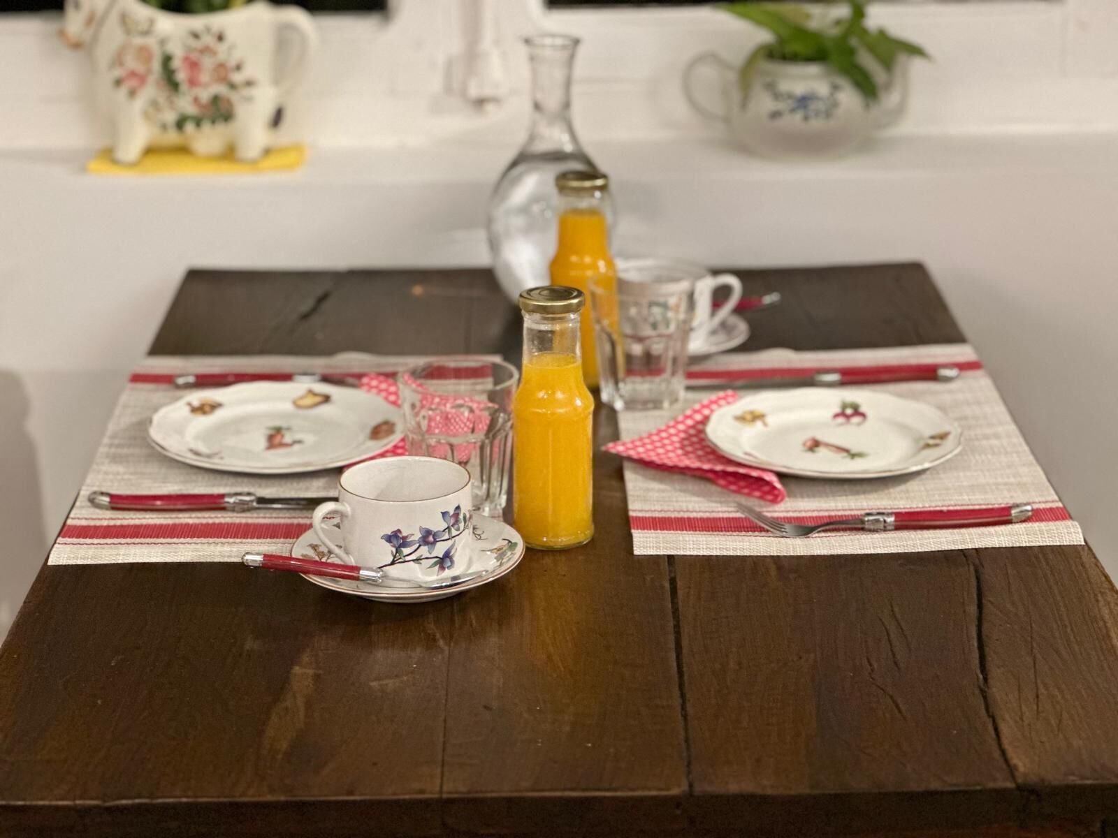 A breakfast table set with plates, a cup, a glass pitcher, and a bottle of orange juice.