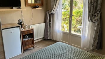 Un dormitorio con una cama, televisor, refrigerador pequeño, armario de madera y ventana con cortinas.