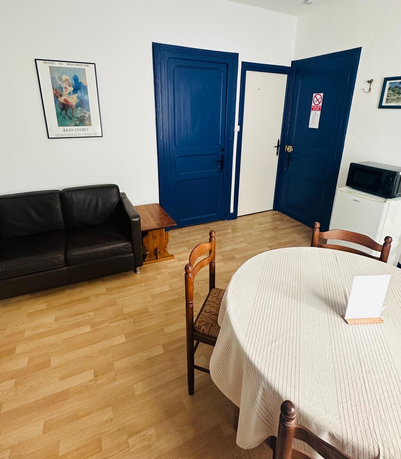 Una habitación con un sofá de cuero negro, una mesa de comedor de madera con mantel blanco, una silla de madera y una puerta azul.