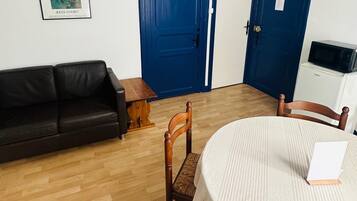 Una habitación con un sofá de cuero negro, una mesa de comedor de madera con mantel blanco, una silla de madera y una puerta azul.