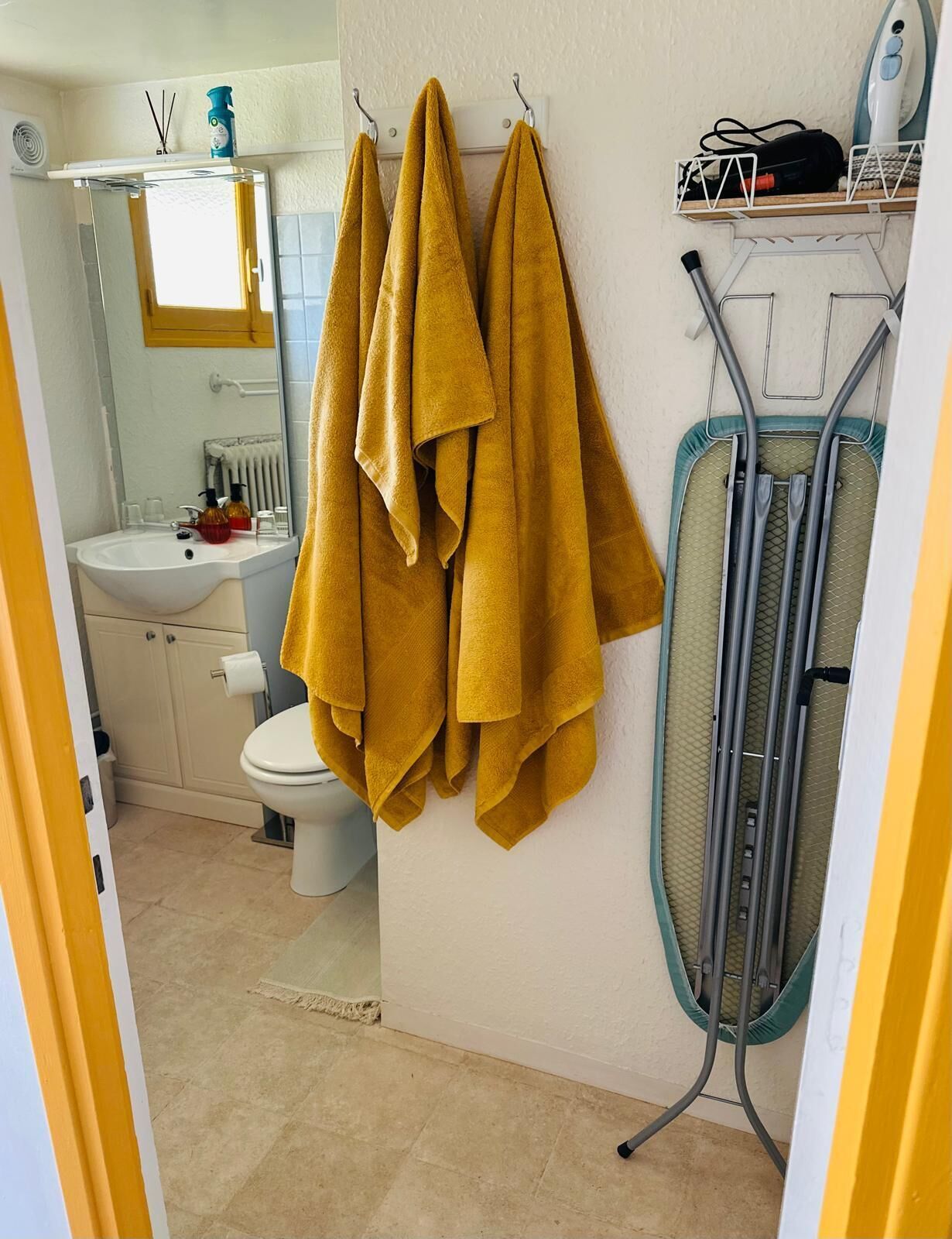 A bathroom with a sink, toilet, mirror, and an iron stand.