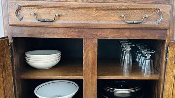 A wooden cabinet with two drawers and two shelves, containing bowls, plates, and glassware.