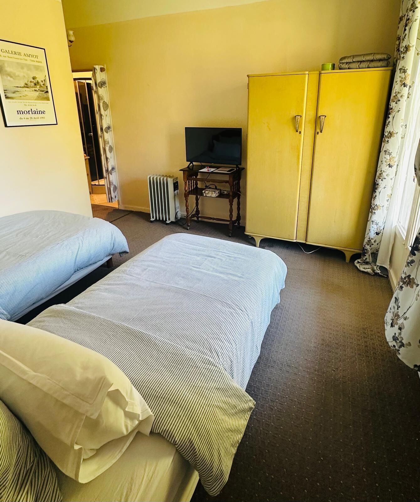 Een hotelkamer met twee bedden, een televisie, een radiator en een gele kast.
