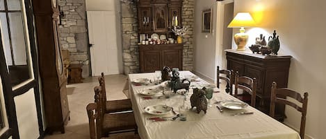 A dining area with a table set for four, surrounded by wooden chairs. A stone wall and a wooden cabinet with decorative items are visible in the background.