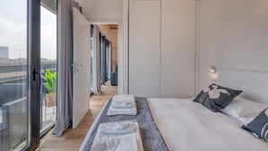 Ein modernes Hotelzimmer mit einem großen Bett, einem Balkon mit Blick und einer Schiebetür zu einem Flur.