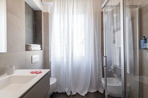 Een moderne badkamer met een glazen douchecabine, een witte wastafel en een toilet.