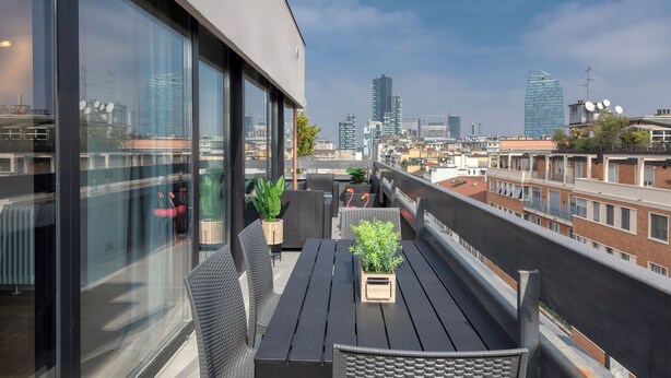 Eine Dachterrasse mit Holztisch und -stühlen, Topfpflanzen und Blick auf die Stadt.