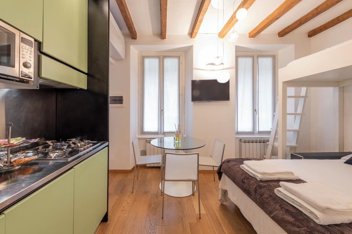 Quarto compacto com cozinha compacta, área de refeições com mesa de vidro e cama com cobertor marrom.