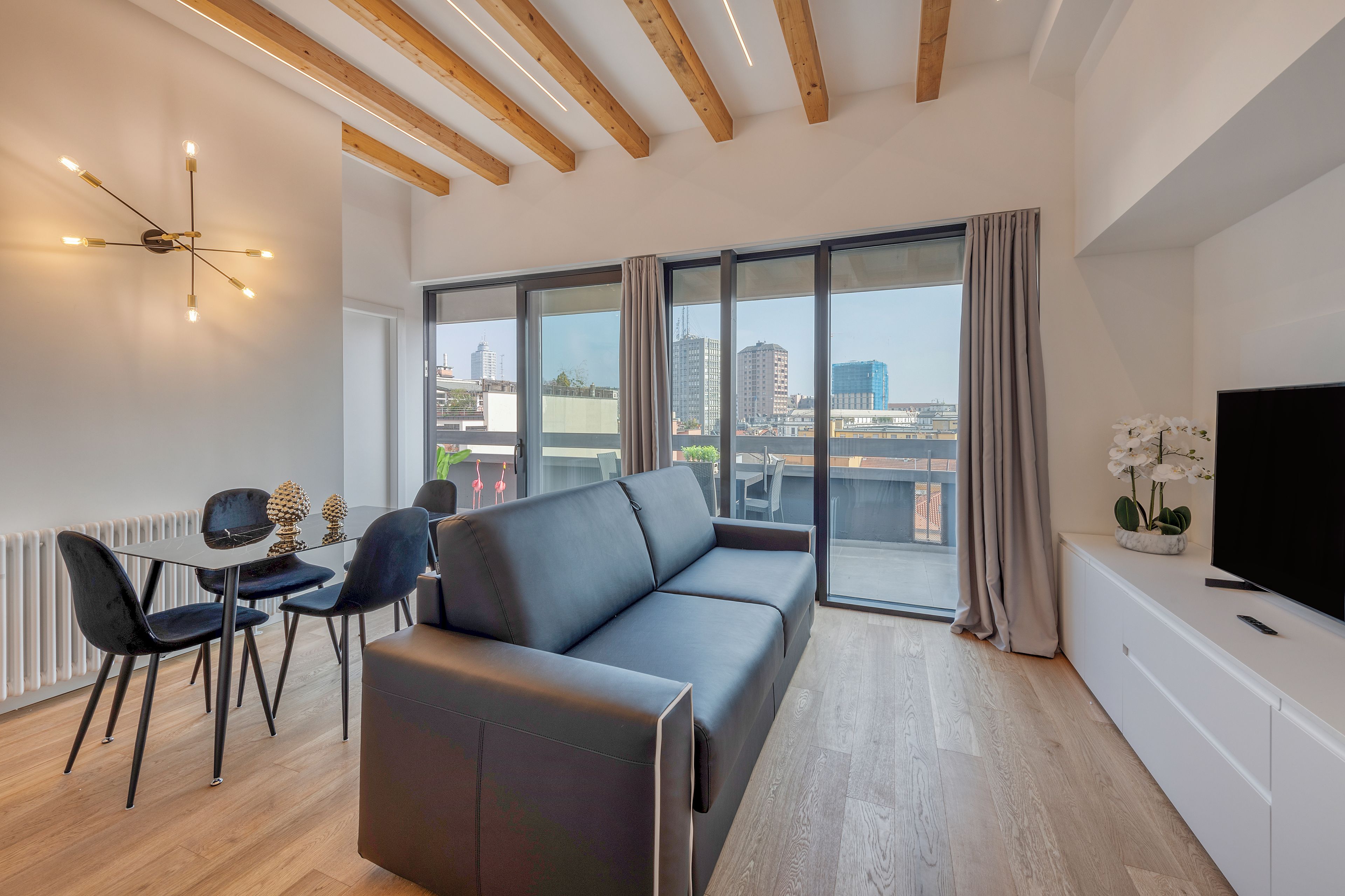 Een moderne woonkamer met een bank, stoelen, een televisie en een groot raam met uitzicht op de stad.