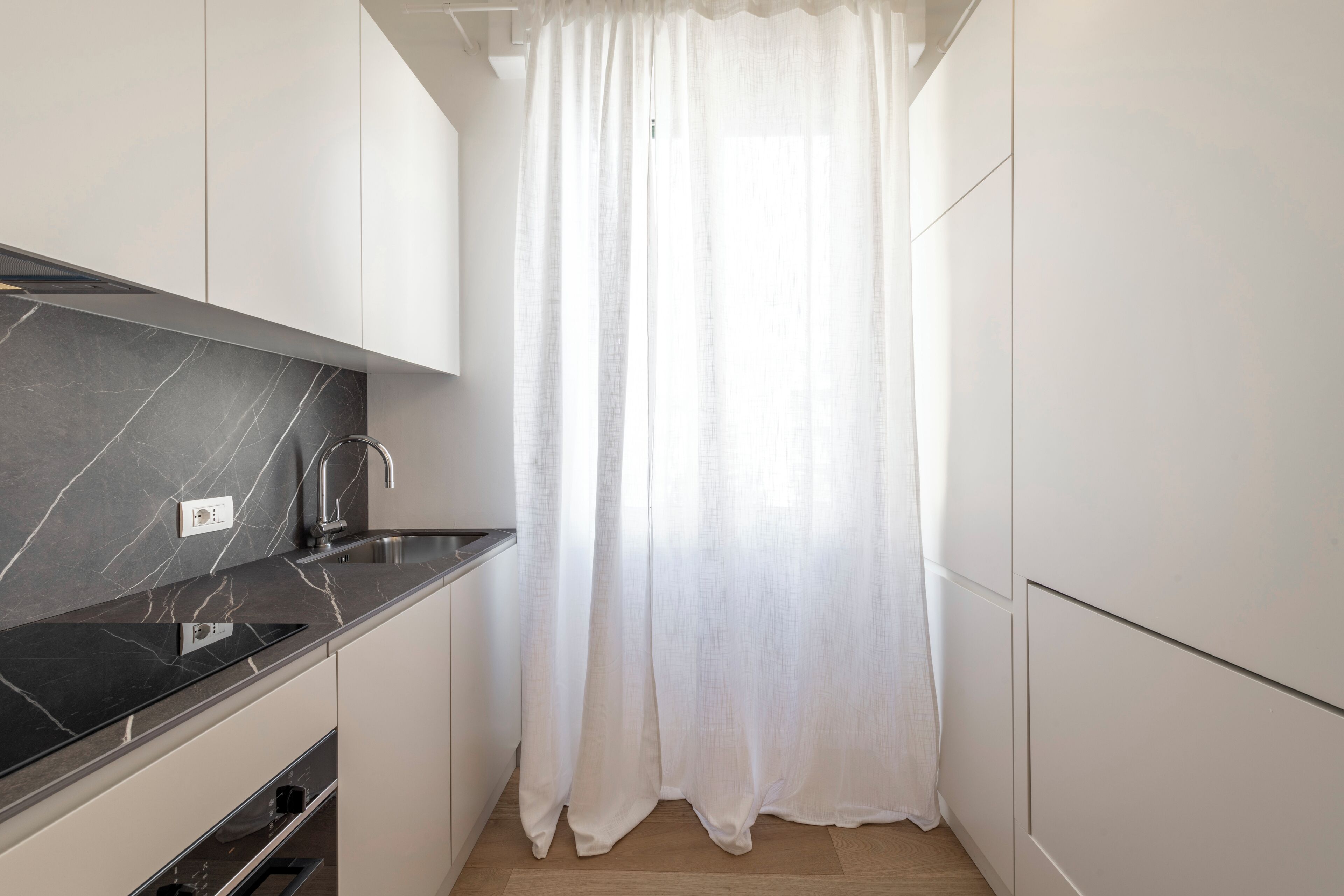 Een moderne keuken met witte kastjes, een zwart marmeren aanrechtblad en een roestvrijstalen spoelbak.