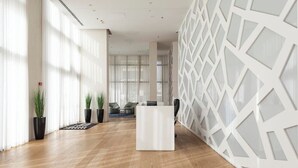 A modern interior with a reception desk, wooden flooring, potted plants, and a geometric wall design. - Luxury Apt Tower | Sea View Bat Yam | Mamad (Bat Yam)