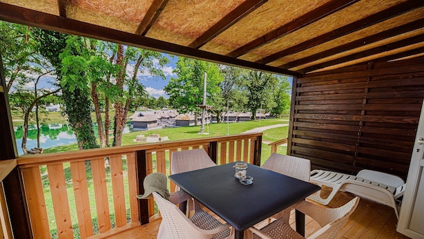 A covered outdoor seating area with a table and chairs, overlooking a lake and residential buildings.