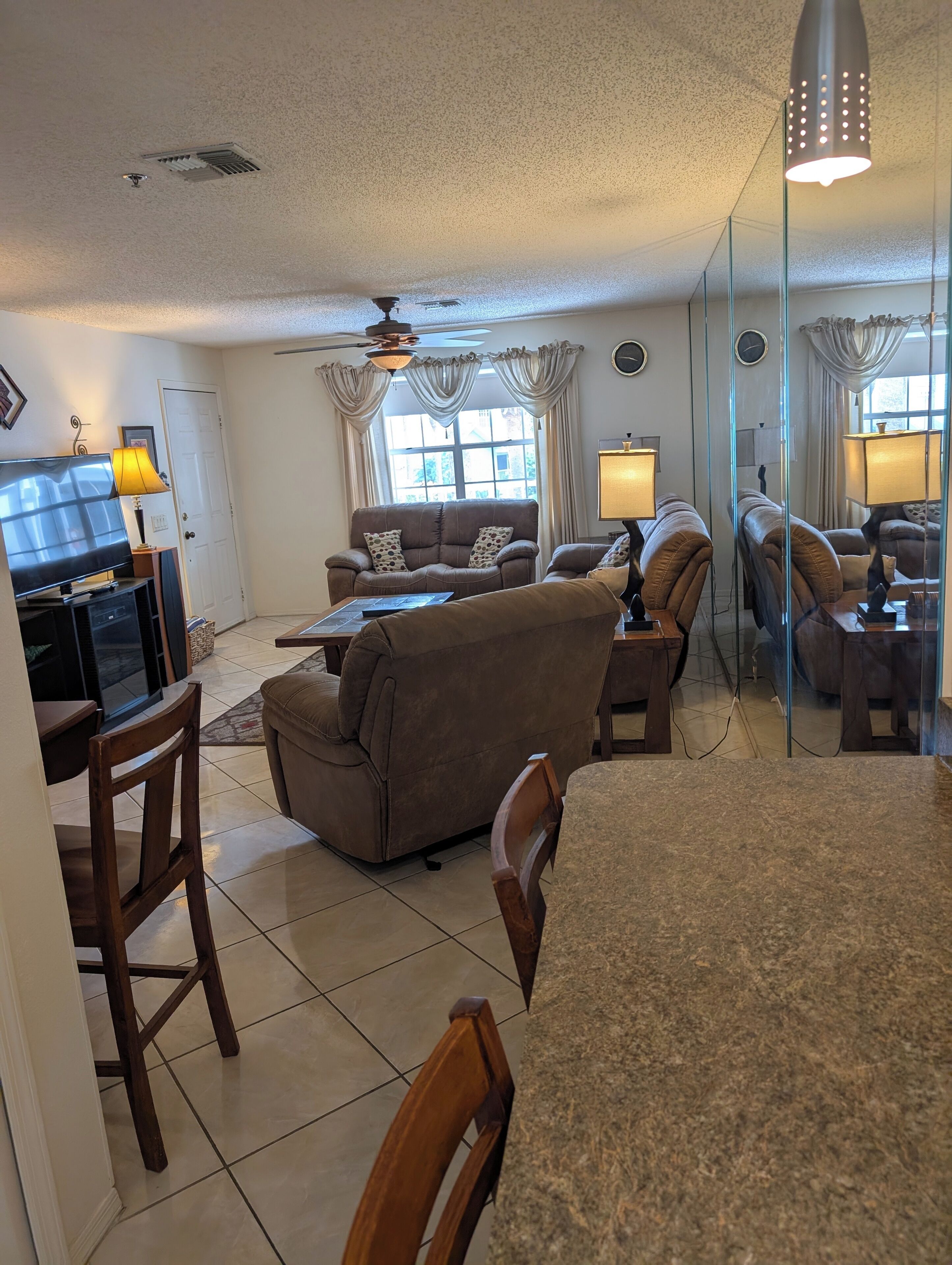 A living room with a sofa, chairs, a TV, a ceiling fan, and a large window with curtains.