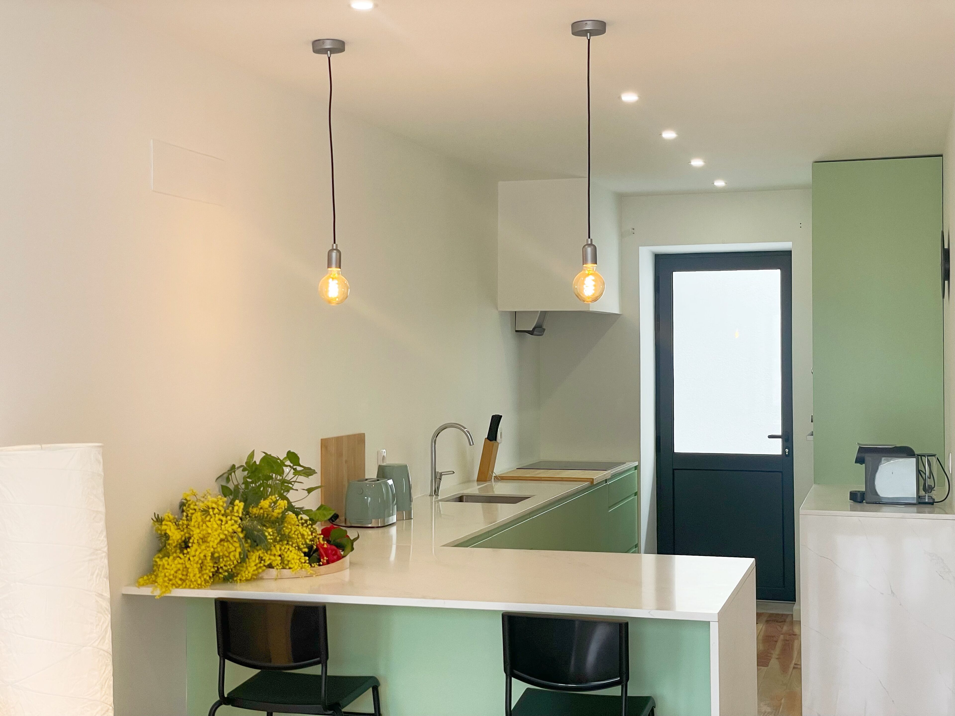 A modern kitchen with a central island, pendant lights, and a view into the adjacent room.