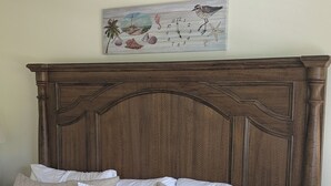 Ein Bett mit einer gesteppten Matratze, einem Holzkopfstück und einem Wandbild mit einer Strandansicht.