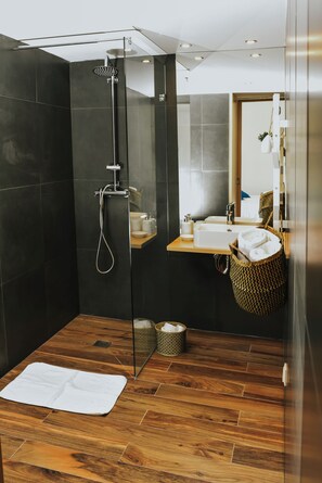A modern bathroom with a glass-enclosed shower, a wooden floor, a sink with a mirror, and a towel rack. - Spacious 50 m² private suite for up to 5 guests, with king bed, three single beds, bathroom and equipped kitchenette. Shared seasonal pool, garden, barbecue, fire pit and telescope. Free gated parking. Pets: €7/night. (Covilhã -Peso)