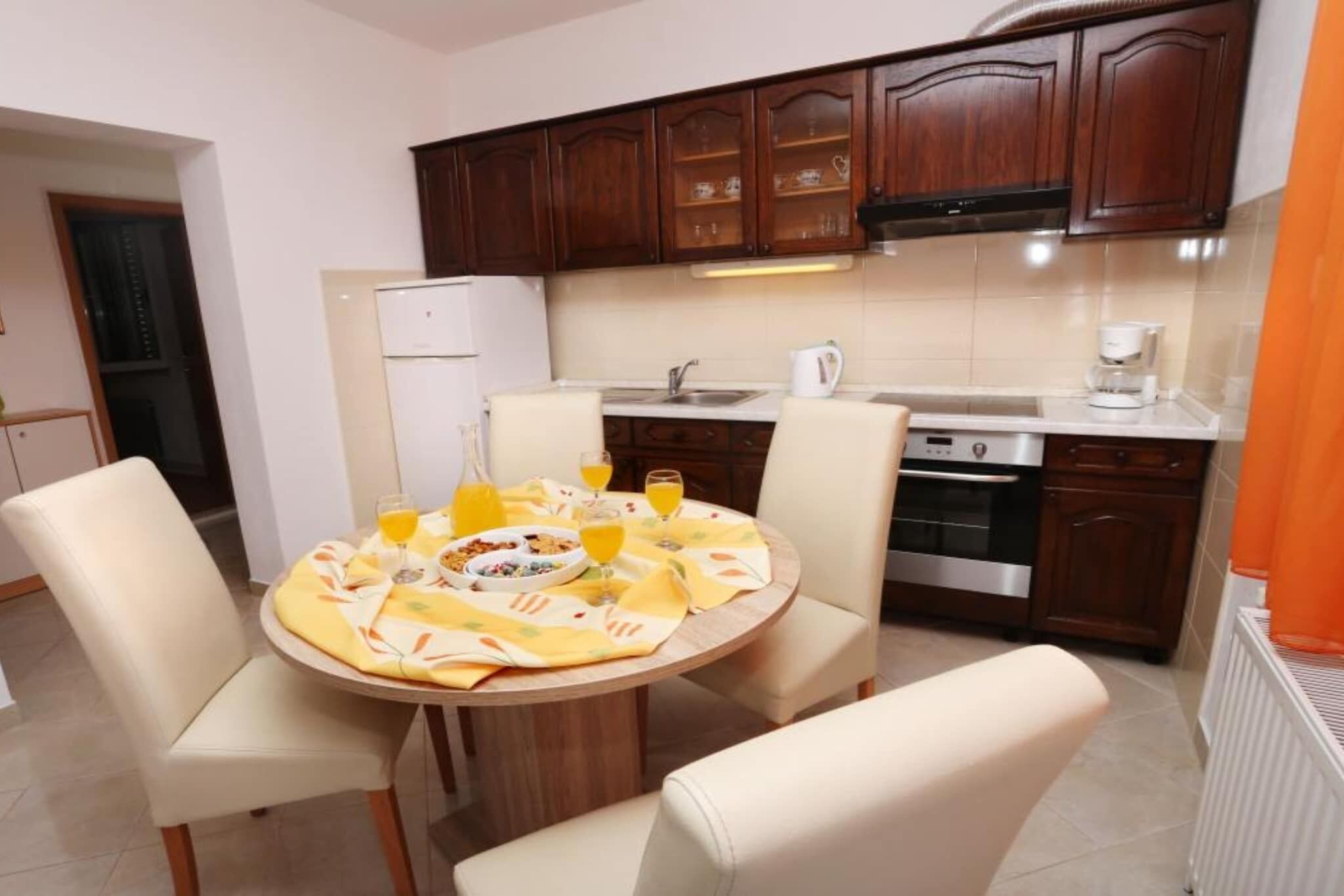 A modern kitchen with wooden cabinets, a stainless steel refrigerator, and a dining area with a round table and chairs.
