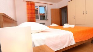 A bedroom with a bed, a wooden wardrobe, a window with curtains, and a door. - One-Bedroom Apartment With Terrace (A2) (Trogir)