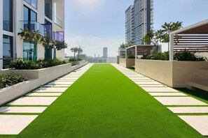 Eine Dachterrasse mit Kunstgrasanlage, modernen Gebäuden und Palmen.