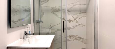 A modern bathroom with a marble backsplash, a glass shower enclosure, and a wooden vanity.