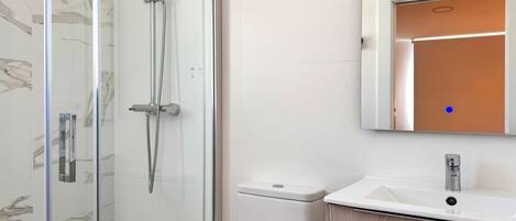 A modern bathroom with a glass shower enclosure, a white sink, and a mirror above it.