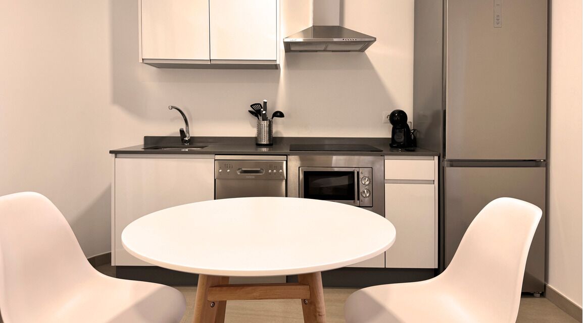 Cocina moderna con lavavajillas, horno y refrigerador. Hay una mesa redonda con dos sillas.