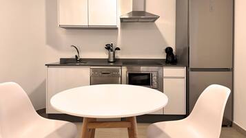 Cocina moderna con lavavajillas, horno y refrigerador. Hay una mesa redonda con dos sillas.
