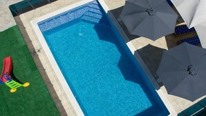 A rectangular swimming pool with a clear blue water surface, surrounded by a tiled deck and a green lawn area.