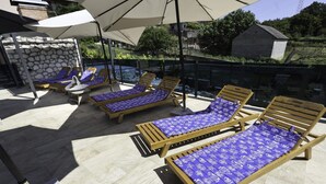A rooftop terrace with wooden lounge chairs and umbrellas, stone walls, and a view of the surrounding landscape.