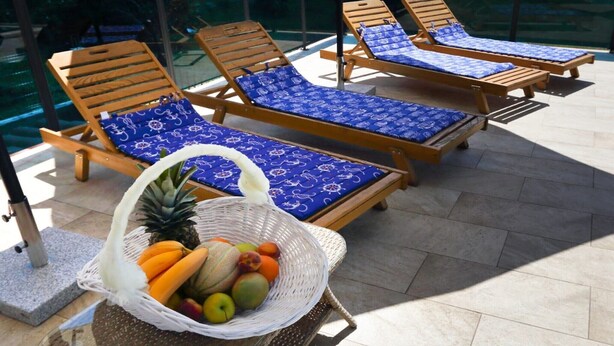 A poolside area with wooden lounge chairs and a wicker basket filled with fruits.