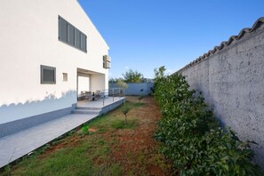 Um pátio com um edifício branco, um pequeno jardim e um muro.