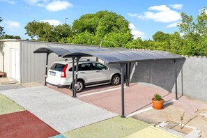 Um carro estacionado sob uma cobertura, com um vaso de planta por perto.