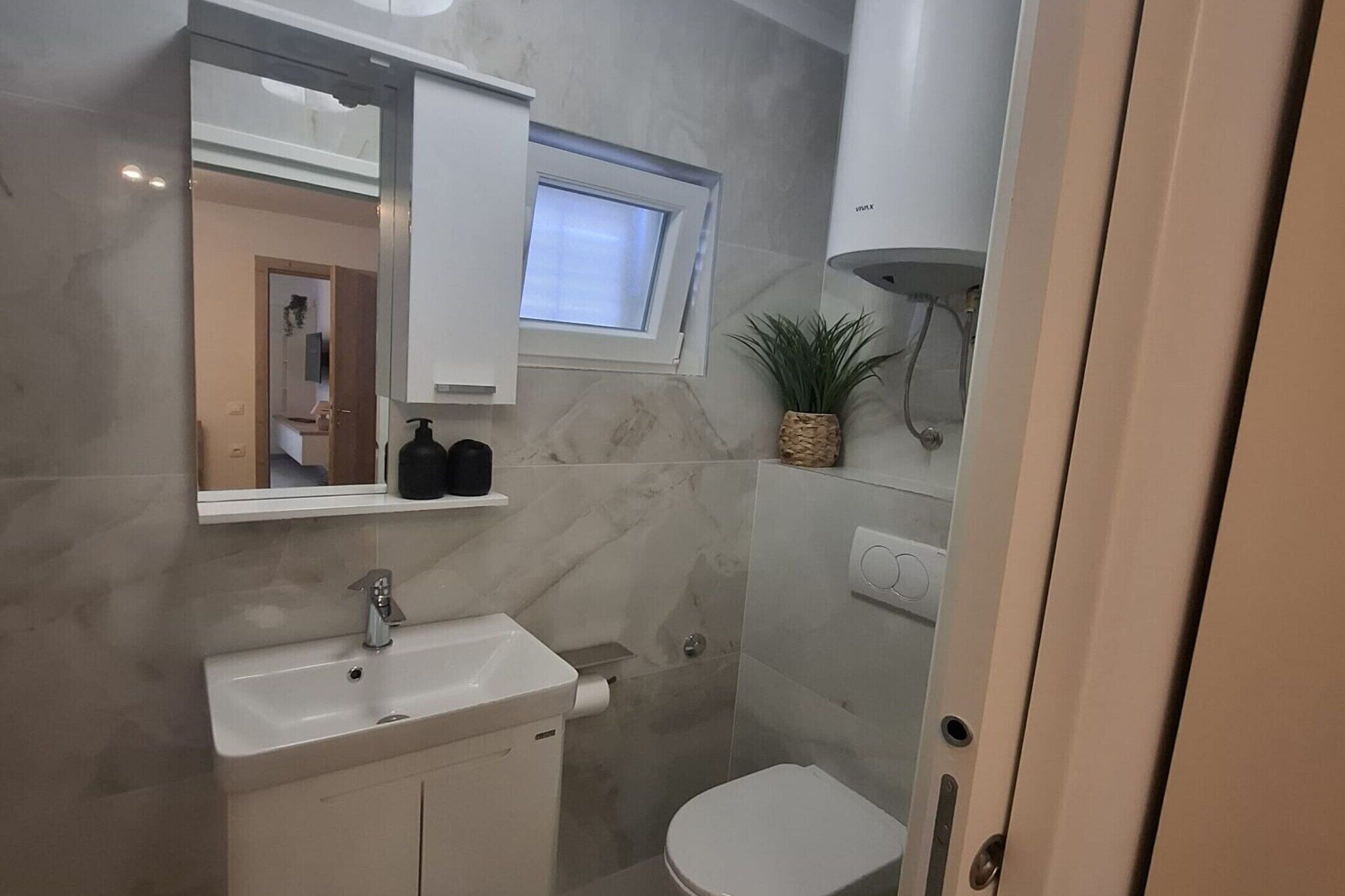 Un baño moderno con un lavamanos blanco, un espejo, una ventana y un inodoro.