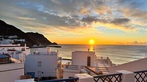 A coastal sunset view with buildings in the foreground and a mountainous backdrop. - Apartamentos Vela Blanca (San José)