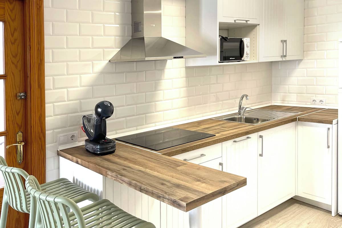 A modern kitchen with white cabinetry, a wooden countertop, a built-in microwave, and a stainless steel sink.