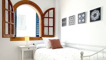 A bedroom with a bed, a bedside table with a lamp, a window with wooden shutters, and four wall-mounted decorative plates.