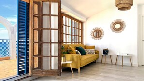 Un salon avec un canapé jaune, une porte en bois et une vue sur l’extérieur.