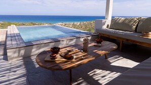 Un espace aménagé au bord de la piscine avec vue sur l’océan, une table en bois avec des collations et un coin salon confortable.