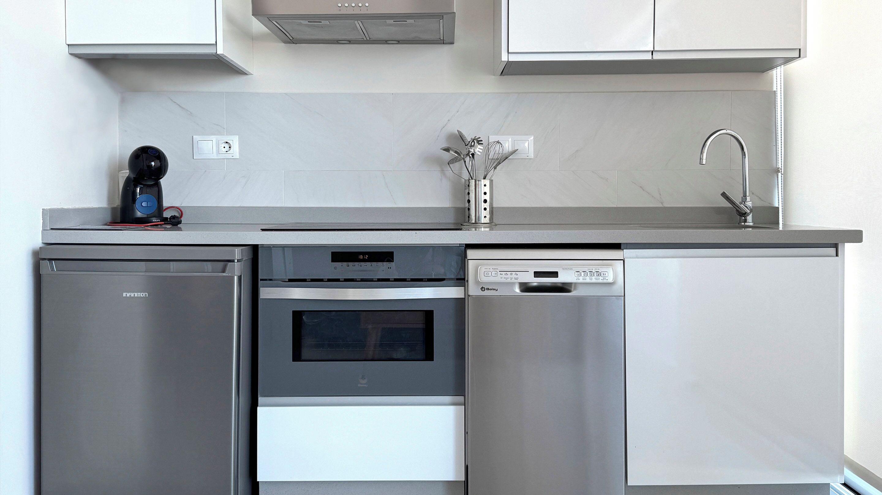 A compact kitchen with a refrigerator, oven, dishwasher, and a coffee maker on the countertop.